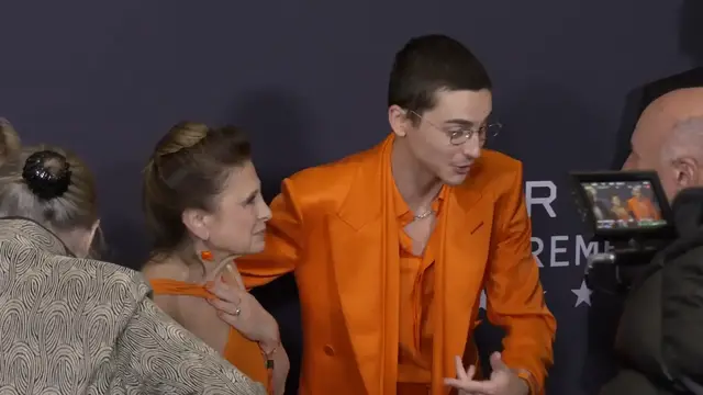 Video thumbnail for Timothée Chalamet and his mom match in 'Marty Supreme' orange on NYC premiere red carpet